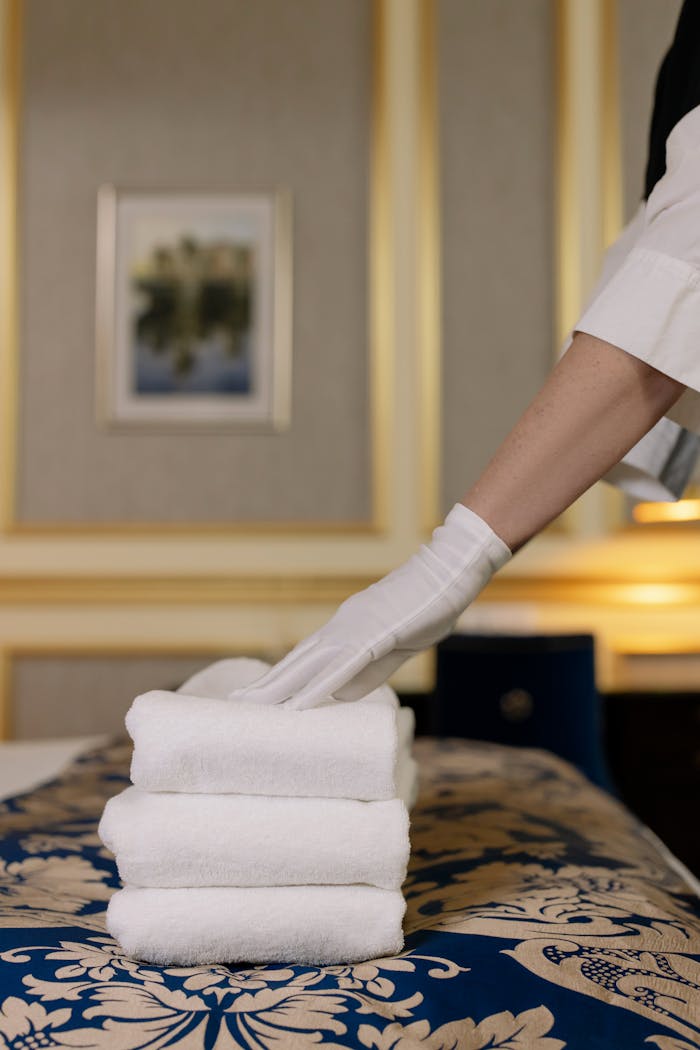 about-02 A hotel housekeeper in uniform arranges freshly laundered towels in a luxurious room.